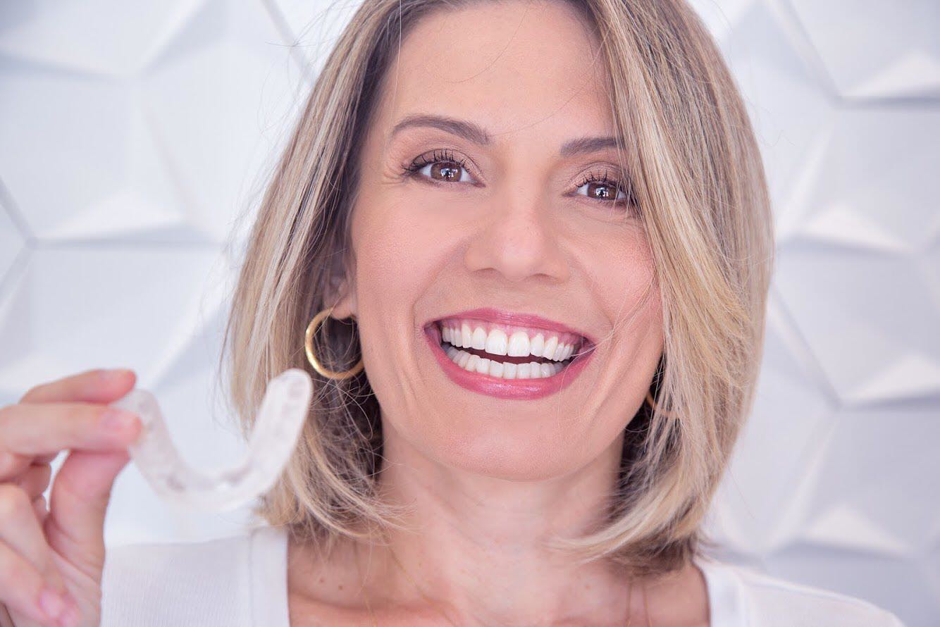 Paciente sorrindo, segurando um alinhador transparente